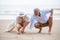 senior couple sitting on the beach drawing a heart in the sand together ,  woman asian man caucasian