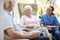 Senior Couple Sitting In Chair And Talking With Nurse In Retirement Home