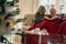 Senior couple sitting on a sofa enjoying reading a book with a gift box in the foreground. Smiling couple spending time together