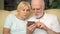 Senior couple sitting on sofa at home. Modern pensioners using mobile, browsing, reading news