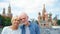 Senior couple stand on background of St. Basil`s Cathedral and Kremlin clock tower in Moscow, Russia