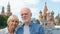 Senior couple stand on background of St. Basil`s Cathedral and Kremlin clock tower in Moscow, Russia