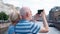 Senior couple stand on embankment of canal take pictures on mobile phone in Saint Petersburg, Russia