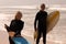 Senior couple with surfboard standing on beach and looking at camera