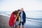 Senior couple and their preteen granddaughter hugging when walking on sandy beach.