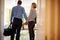 Senior couple walk in to hotel room holding hands, back view