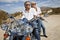 Senior couple wear sunglasses seated on motorcycle on desert road