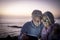 A senior couple white-haired looking at digital tablet in the dusk sitting on the beach with horizon over water on background.