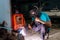 Senior Craftsman, wearing a welding helmet, sitting very skilled and careful welding, on his chair in a small factory