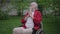 Senior disabled man in wheelchair praying outdoors in green spring garden. Portrait of hopeful Caucasian handicapped