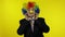 Senior elderly clown businesswoman boss in wig adjusts tie. Yellow background