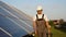 Senior engineer in protective workwear walking and examining photovoltaic panels at solar power plant