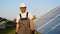 Senior engineer in protective workwear walking and examining photovoltaic panels at solar power plant
