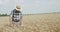 Senior farmer in hat walks in wheat spacious field, looks at sky and rejoices