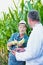 Senior farmer standing and showing corn whilst crop scientist holding digital tablet against corn plant