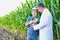 Senior farmer standing and showing corn whilst crop scientist holding digital tablet against corn plant