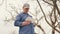 Senior farmer with a tablet inspects fruit trees in spring. The gardener examines the branches of an apple tree in