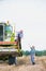 Senior farmer talking to mature farmer standing on harvester in field