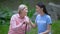 Senior female patient with walking stick talking young volunteer sitting outdoor