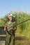 Senior fisherman catches fish on river bank in reeds. Retired fishing in summer. Bright sunlight, soft focus