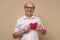 Senior gentleman in glasses holding a red heart smiling.