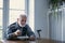 Senior grandfather with grey hair and beard sitting alone in the kitchen eating breakfast