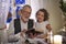 Senior grandfather with small granddaughter indoors at Christmas, reading Bible.