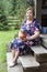 Senior grandma holding stoneware jug in hands while sitting on wooden stair of porch, timber house in countryside area