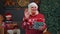 Senior grandmother in Christmas sweater smiling friendly at camera and waving hands gesturing hello