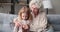 Senior grandmother teaching cute granddaughter knitting together on sofa