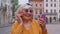 Senior grandmother woman tourist with smartphone, smiling, listening music in app wearing earphones