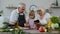 Senior grandparents couple with digital tablet and granddaughter cutting vegetables in kitchen