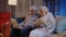 Senior grandparents couple reading book, using laptop pc on couch in night living room at home