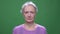 Senior gray haired woman in violet sweater turns head negatively isolated on green chromakey background.