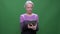 Senior gray haired woman in violet sweater works with tablet isolated on green chromakey background.