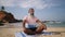 Senior grey bearded traveler use meditation practice and yoga to clear mind, sitting in lotus pose on tropical island