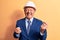 Senior grey-haired architect man wearing suit and security hardhat over yellow background celebrating surprised and amazed for