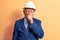 Senior grey-haired architect man wearing suit and security hardhat over yellow background feeling unwell and coughing as symptom