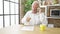 Senior grey-haired man angry arguing on smartphone sitting on table at dinning room