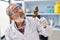 Senior grey-haired man scientist holding cannabis herb with tweezers at laboratory