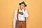 Senior grey-haired man wearing german traditional octoberfest suit over yellow background thinking looking tired and bored with