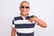 Senior grey-haired man wearing striped polo and sunglasses over isolated white background with surprise face pointing finger to