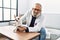 Senior grey-haired man wearing veterinarian uniform examining chihuahua at vet clinic