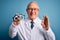 Senior grey haired optic doctor man holding optometrist eyeglasses over blue background doing ok sign with fingers, excellent