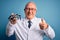 Senior grey haired optic doctor man holding optometrist eyeglasses over blue background happy with big smile doing ok sign, thumb