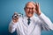 Senior grey haired optic doctor man holding optometrist eyeglasses over blue background with happy face smiling doing ok sign with