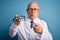 Senior grey haired optic doctor man holding optometrist eyeglasses over blue background pointing with finger to the camera and to