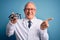 Senior grey haired optic doctor man holding optometrist eyeglasses over blue background very happy pointing with hand and finger