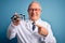 Senior grey haired optic doctor man holding optometrist eyeglasses over blue background very happy pointing with hand and finger