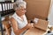 Senior grey-haired woman business worker scanning package label at office